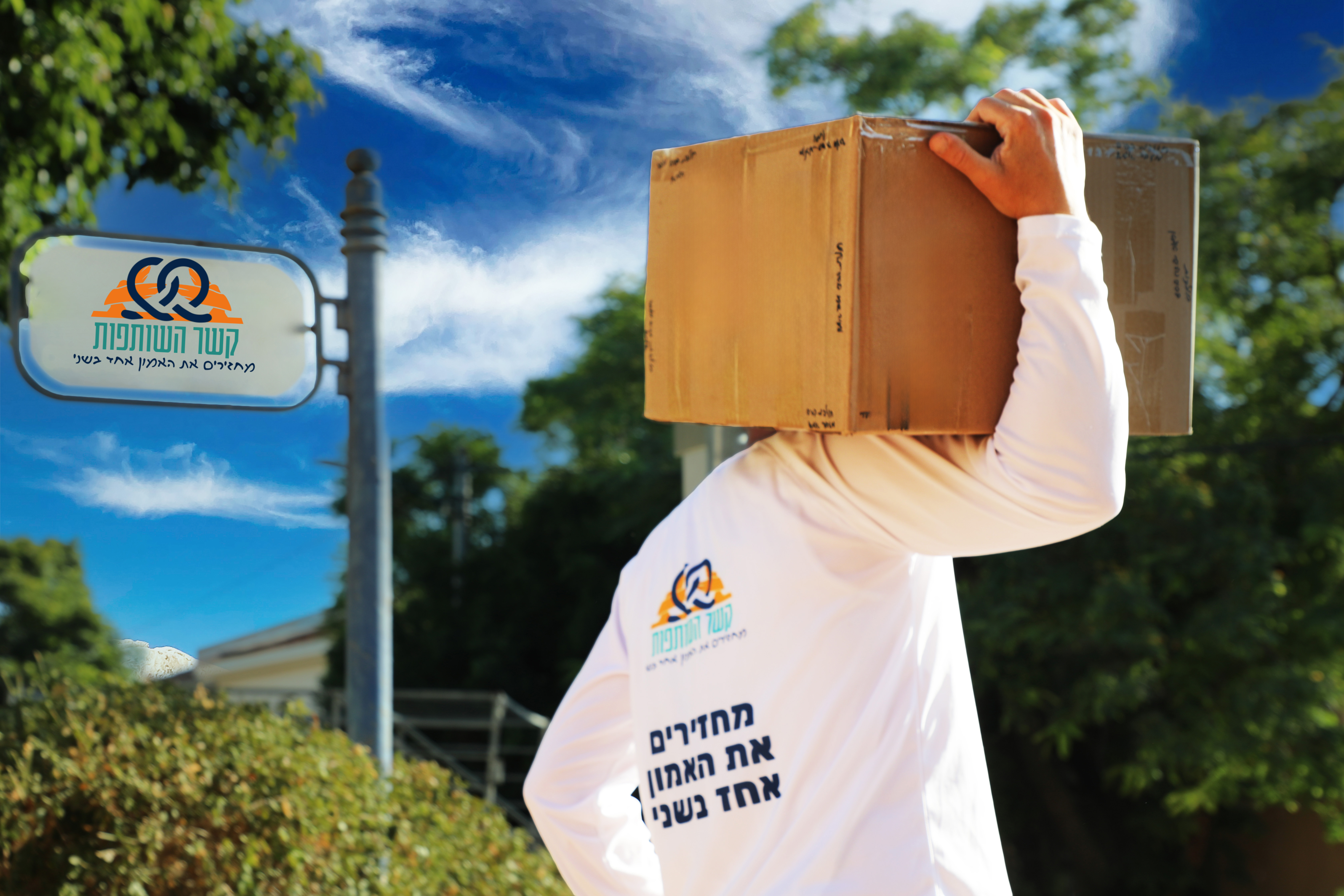 נשיאת חבילת סיוע במסגרת פעילות קשר השותפות, לצד שלט העמותה